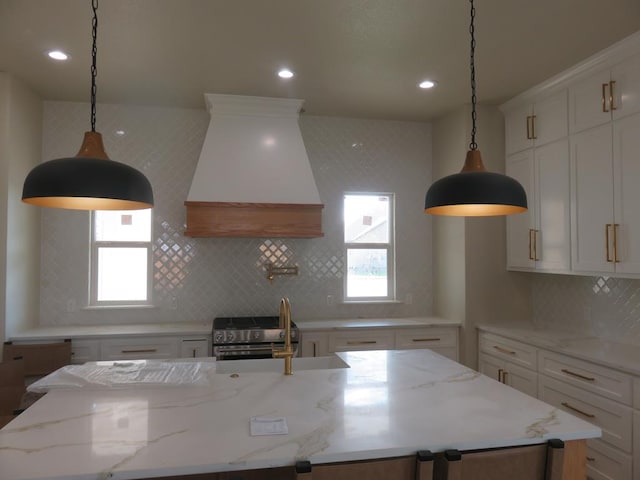 kitchen featuring custom exhaust hood, white cabinetry, stainless steel range with gas stovetop, backsplash, and a center island with sink