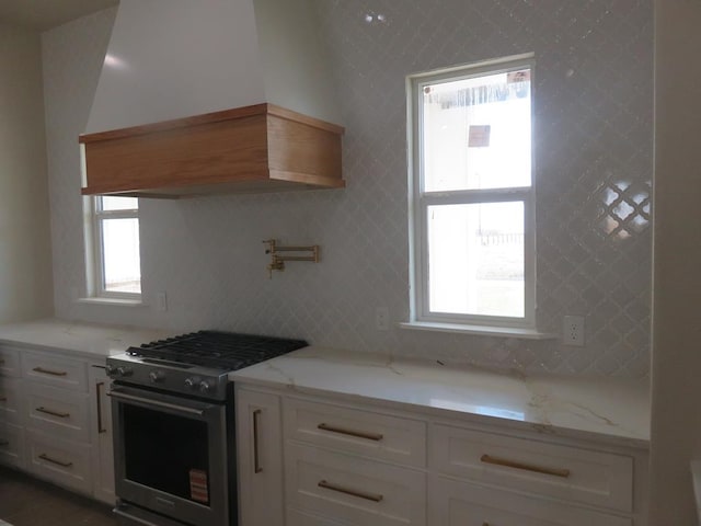 kitchen with white cabinetry, stainless steel gas stove, custom exhaust hood, and light stone countertops