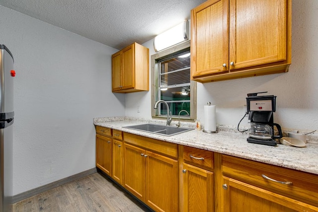 707 E County Rd 132, Midland, TX 79706 - kitchen with a sink, light wood-style floors, baseboards, a textured ceiling, and brown cabinetry