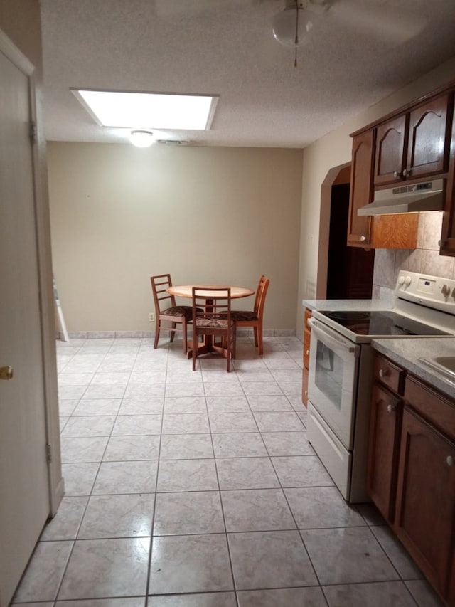 1607 E Pecan Ave, Midland, TX 79705 - kitchen with under cabinet range hood, white electric range oven, tasteful backsplash, light tile patterned floors, and a skylight