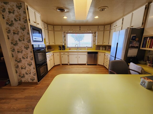 kitchen featuring white cabinets, light wood-type flooring, stainless steel appliances, and a textured ceiling