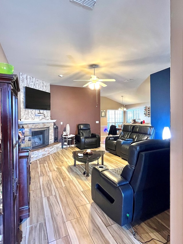 living room with a fireplace, ceiling fan with notable chandelier, wood-type flooring, and vaulted ceiling