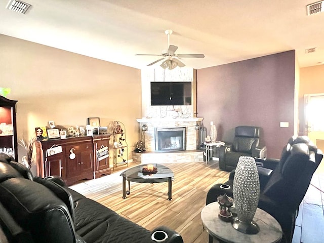 living room featuring a stone fireplace, ceiling fan, and light hardwood / wood-style floors