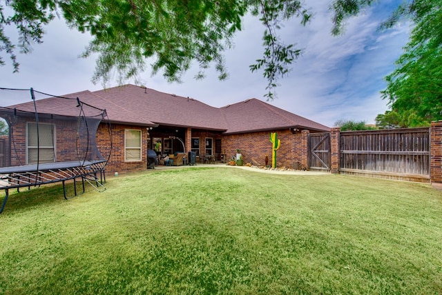 back of house featuring a trampoline, brick siding, a shingled roof, and a patio area