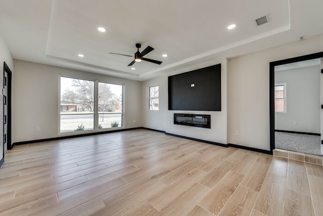 unfurnished living room with a tray ceiling, light wood finished floors, and visible vents