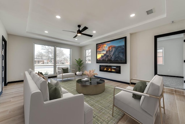 interior space with light wood finished floors, a raised ceiling, a healthy amount of sunlight, and visible vents