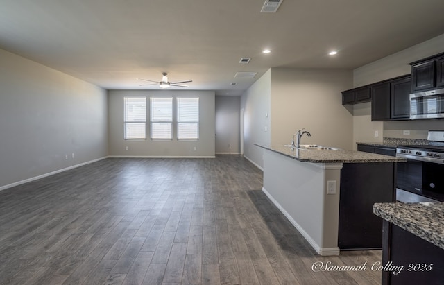 kitchen with sink, appliances with stainless steel finishes, light stone counters, a center island with sink, and dark hardwood / wood-style flooring