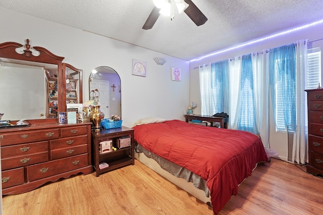 bedroom with arched walkways, a textured ceiling, a ceiling fan, and light wood finished floors