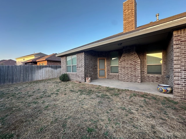 back of house with a patio, a chimney, fence, a yard, and brick siding