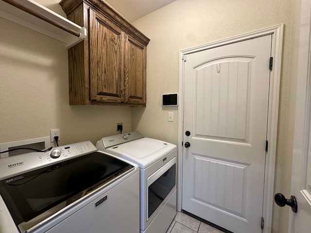 laundry area featuring cabinet space, a textured wall, washing machine and clothes dryer, and light tile patterned floors