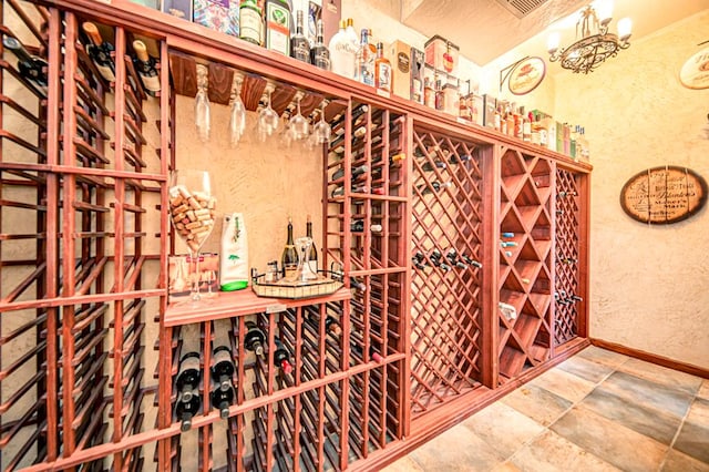 wine area with baseboards, a textured wall, stone finish floor, and an inviting chandelier