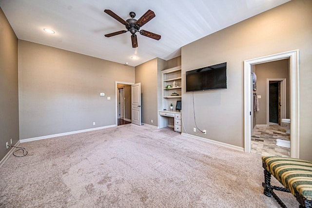 unfurnished living room with light carpet, ceiling fan, built in desk, and baseboards