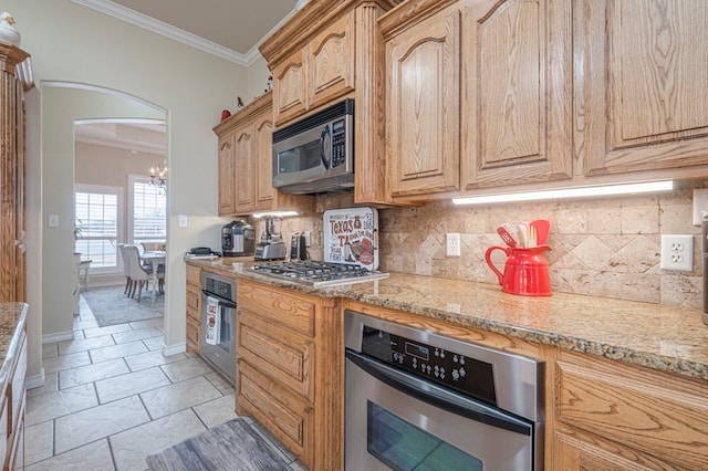 kitchen featuring light stone countertops, crown molding, stainless steel appliances, and backsplash