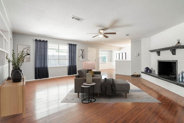 living room with ceiling fan, visible vents, a fireplace, and wood finished floors