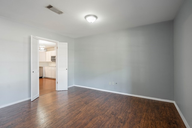 empty room featuring baseboards, visible vents, and dark wood finished floors