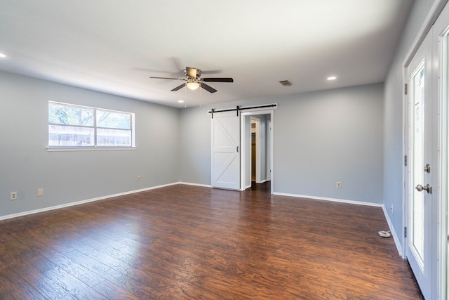 spare room featuring ceiling fan, a barn door, dark wood-type flooring, visible vents, and baseboards