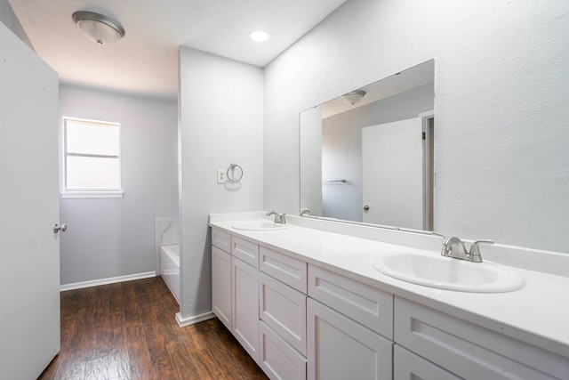 full bathroom featuring double vanity, a garden tub, a sink, and wood finished floors