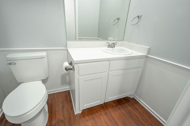 half bath with toilet, wood finished floors, vanity, and baseboards