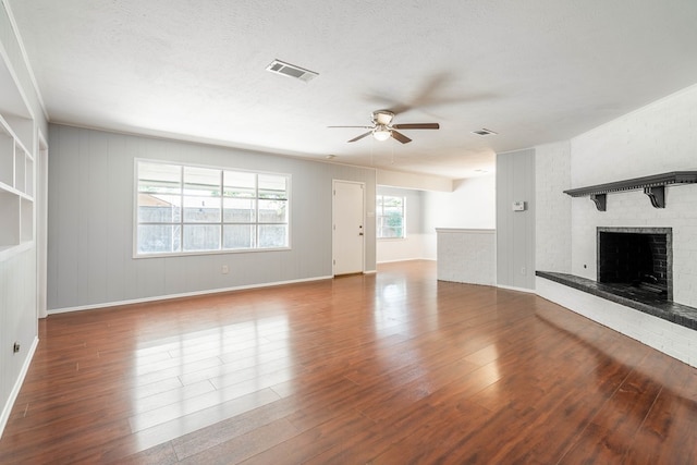 unfurnished living room featuring a textured ceiling, a brick fireplace, wood finished floors, and visible vents