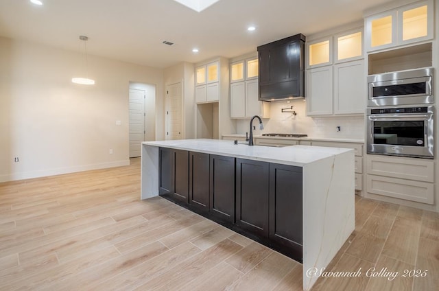 kitchen with light stone countertops, sink, a center island with sink, and light wood-type flooring