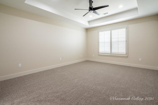 empty room featuring ceiling fan, a raised ceiling, and carpet floors