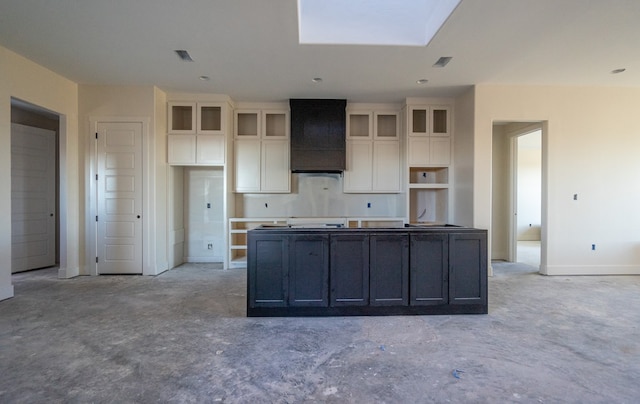 kitchen with a skylight, a center island, white cabinets, and wall chimney exhaust hood