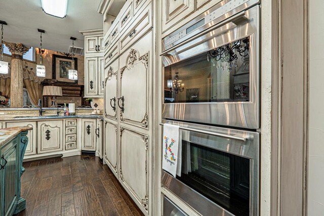 kitchen featuring dark wood finished floors, stainless steel double oven, a sink, and cream cabinetry