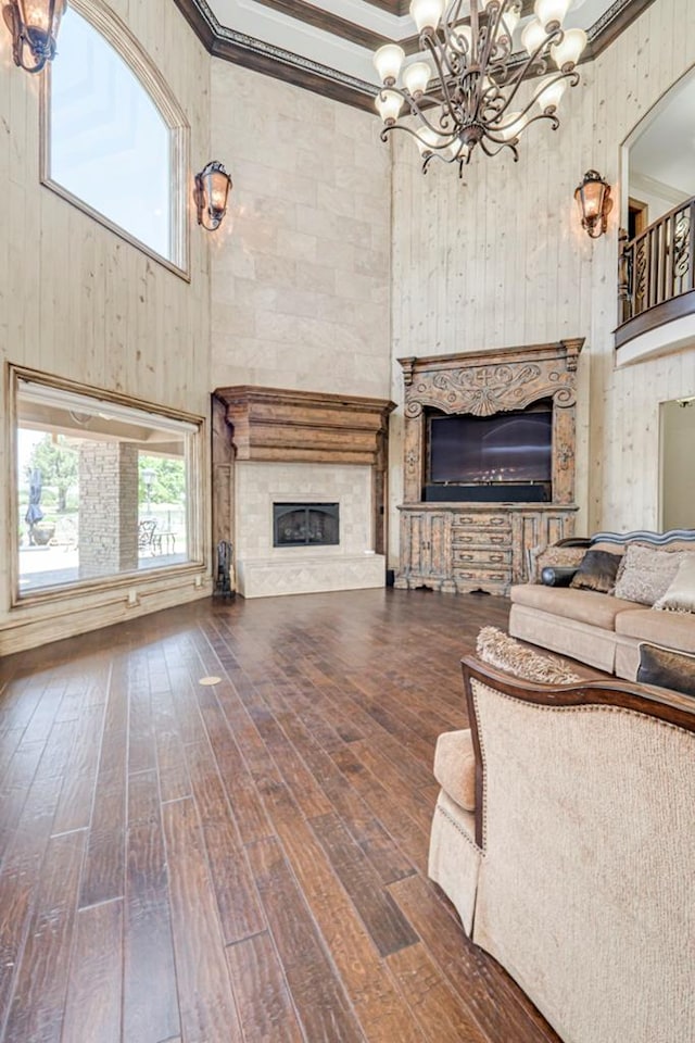 living area featuring an inviting chandelier, a tiled fireplace, hardwood / wood-style flooring, and a towering ceiling