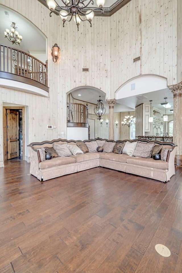 living room with wood walls, a notable chandelier, hardwood / wood-style floors, and a towering ceiling