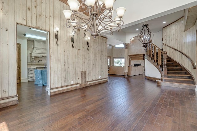 unfurnished living room with wooden walls, a high ceiling, a chandelier, and hardwood / wood-style flooring