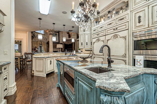 kitchen featuring cream cabinets, light stone counters, appliances with stainless steel finishes, a sink, and dark wood-type flooring