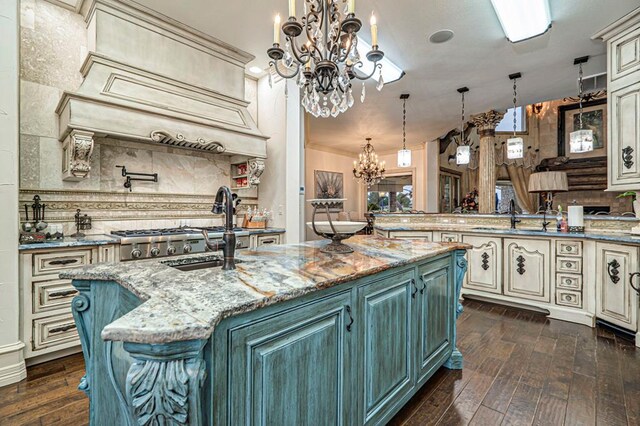 kitchen featuring a kitchen island with sink, backsplash, dark wood-style flooring, an inviting chandelier, and cream cabinetry