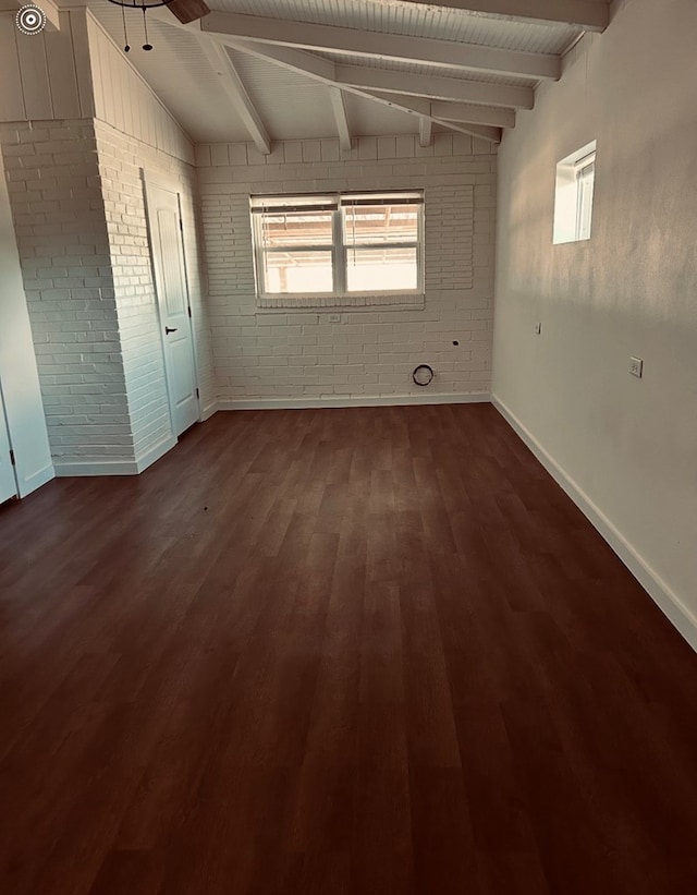 126 Coliseum Dr, Snyder, TX 79549 - empty room featuring lofted ceiling with beams, baseboards, dark wood-type flooring, and brick wall