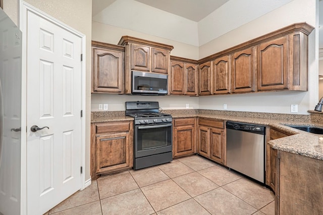 kitchen with light tile patterned flooring, stainless steel appliances, stone countertops, and sink