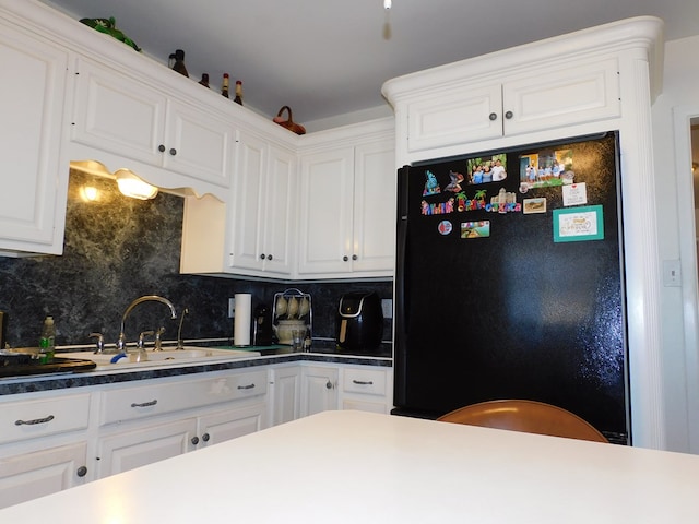 kitchen featuring tasteful backsplash, black fridge, white cabinetry, and sink