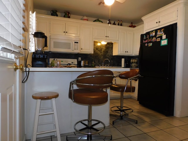 kitchen with black refrigerator, a kitchen bar, tile patterned floors, range, and white cabinetry