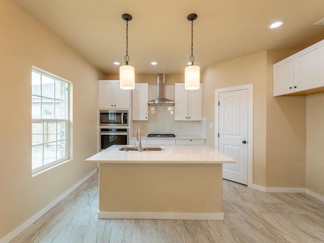 kitchen with wall chimney exhaust hood, appliances with stainless steel finishes, a sink, white cabinetry, and backsplash