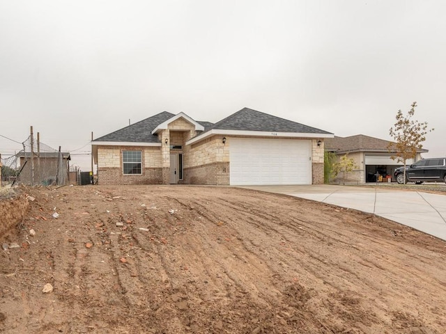 ranch-style home featuring brick siding, roof with shingles, central AC unit, a garage, and driveway