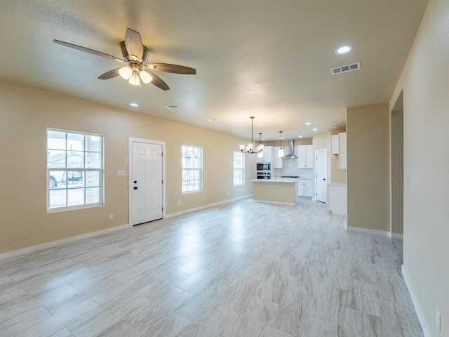 unfurnished living room featuring recessed lighting, visible vents, a textured ceiling, baseboards, and ceiling fan with notable chandelier