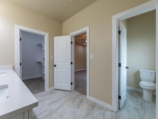 bathroom with a spacious closet, vanity, toilet, and baseboards