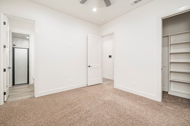 unfurnished bedroom with ceiling fan, a closet, a spacious closet, and light carpet