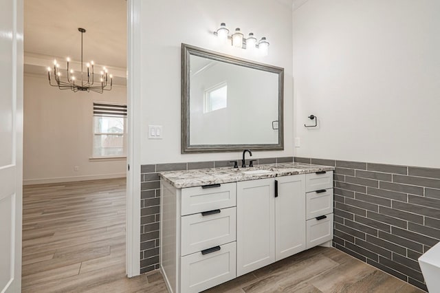 bathroom with an inviting chandelier, vanity, hardwood / wood-style floors, and tile walls