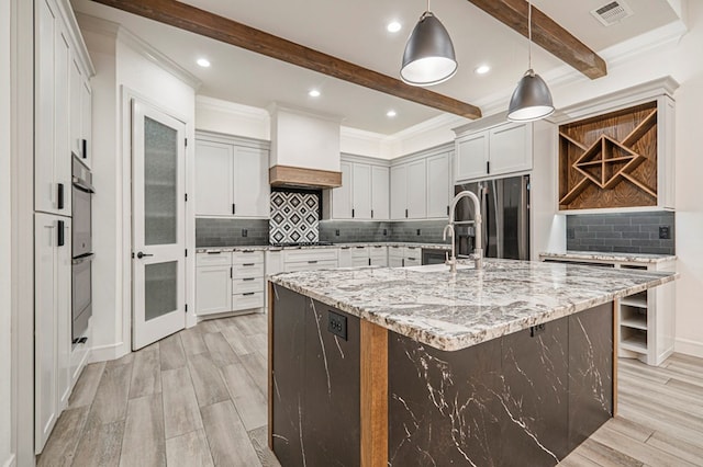 kitchen featuring appliances with stainless steel finishes, pendant lighting, beamed ceiling, light stone counters, and a spacious island