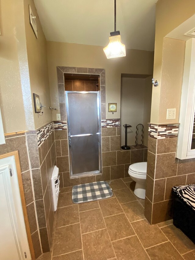 bathroom with tile patterned flooring, toilet, a shower with door, and tile walls