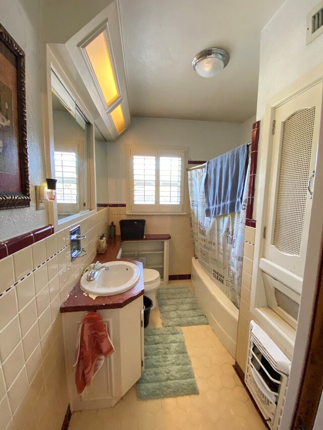 full bathroom with tile patterned floors, toilet, shower / tub combo with curtain, vanity, and tile walls