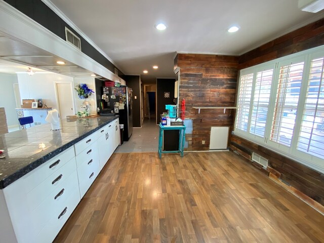 kitchen with stainless steel fridge, wooden walls, white cabinets, and light wood-type flooring