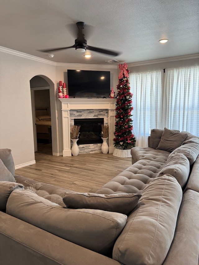 living room with hardwood / wood-style floors, a fireplace, ornamental molding, ceiling fan, and a textured ceiling