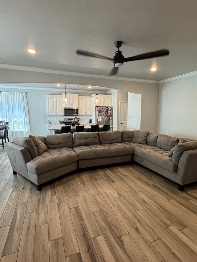 living room featuring crown molding, ceiling fan, and light wood-type flooring