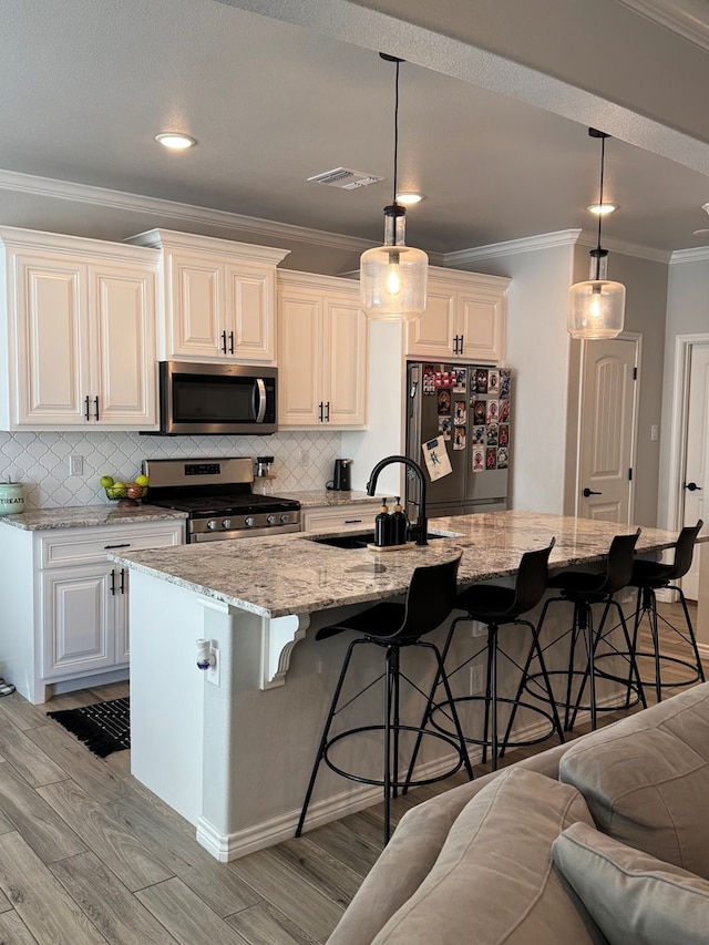 kitchen featuring pendant lighting, a breakfast bar area, appliances with stainless steel finishes, white cabinets, and a center island with sink