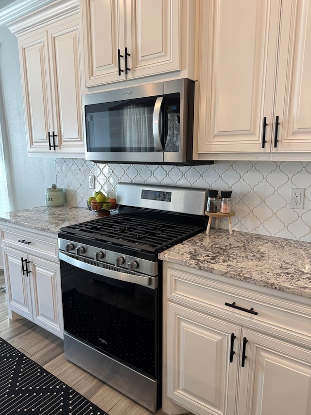 kitchen with white cabinetry, appliances with stainless steel finishes, backsplash, and light stone counters